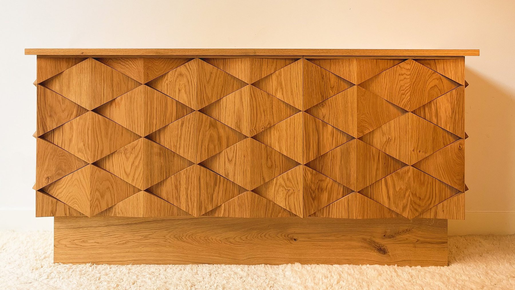 Houten ladekast met een geometrisch patroon op de deuren, geplaatst op een witte tapijtvloer, tegen een lichtgele muur.